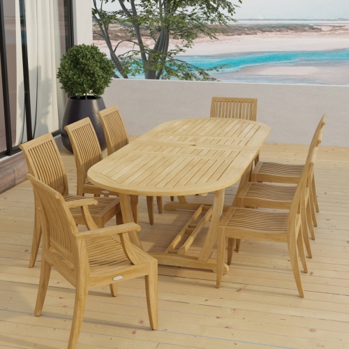 70926 Laguna Montserrat 9 piece Dining Set of Montserrat Oval Teak Table and 2 Laguna Dining Armchairs and 6 Laguna Side Chairs in angled end view on patio with ocean in background