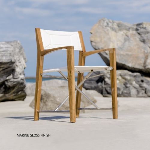 12915F Odyssey Folding Director Chair in marine gloss finish right side angled front facing view on sandy beach by boulder with ocean and blue sky in background