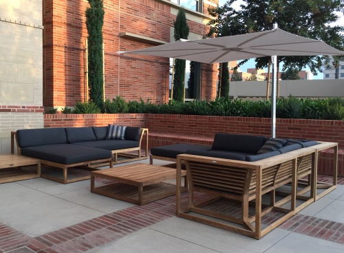 13801dp maya left side sectional with cushions umbrella coffee table ottoman on patio with brick planter with plants trees and brick building background