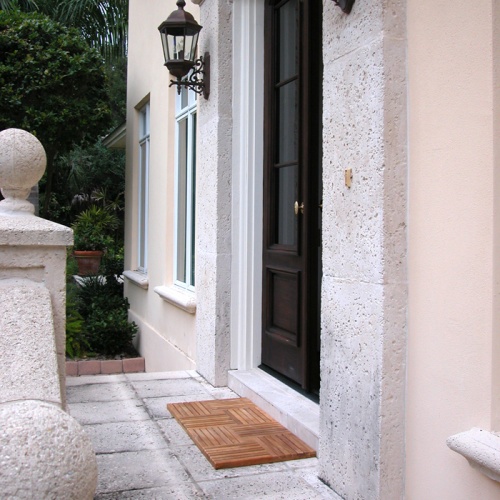 18412DM Parquet Teak Door Mats by an entry door on concrete patio with shrubs in background