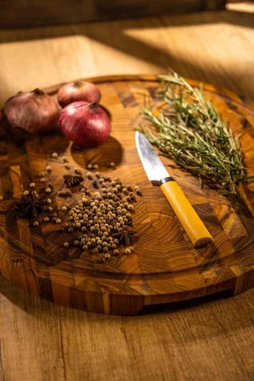 19122 Butcher Block 15 inch Round Charcuterie Cutting Board with rosemary and 3 red onions and whole black pepper and a knife with yellow handle  aerial view on a counter top