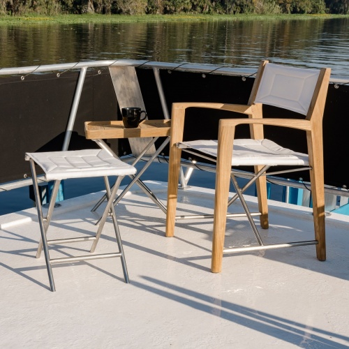 28815F Odyssey Folding Ottoman angled side view with Odyssey armchair and teak side table with coffee cup on boat deck with lake in background