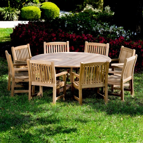 70173 Buckingham 9 pc teak Dining Set with six foot diameter dining table and 8 dining chairs on grass lawn with flowers and tree landscape in background