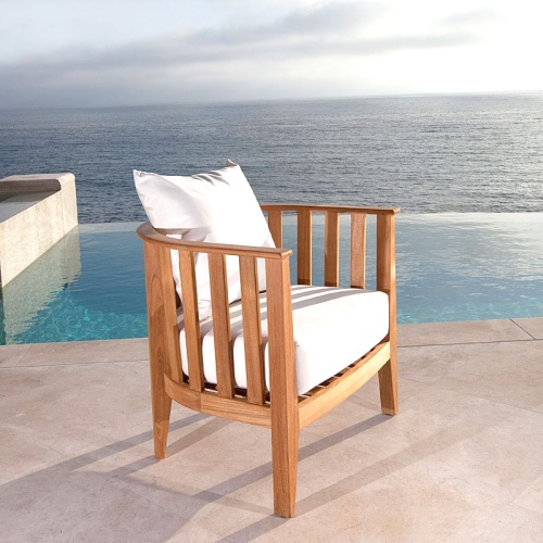 70239 kafelonia teak club chair with cushions side angled on stone patio with pool ocean and blue sky in background
