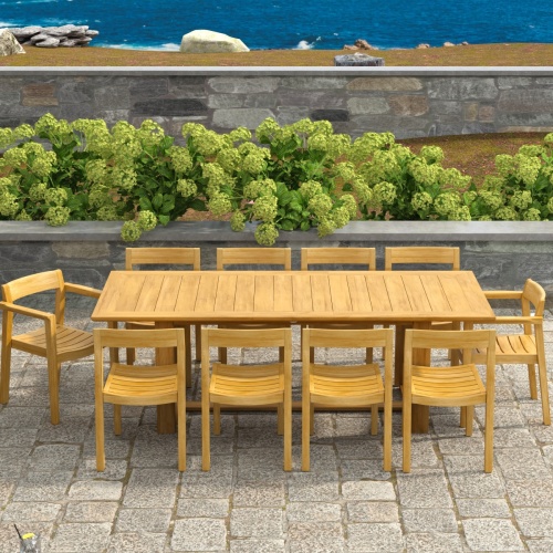 70457 Horizon 11 pc Teak Dining Set of Horizon Rectangular Teak DIning Table and 2 Teak Dining Armchairs and 8 Teak Side Chairs side angled on patio with hillside and ocean background