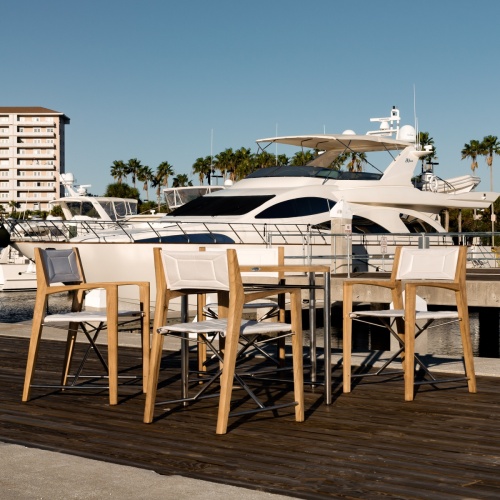 70459 Odyssey 5 Piece folding teak and stainless steel dining set of Odyssey 32 inch square dining table and 4 Odyssey folding chairs on boat dock with yacht and condos in background