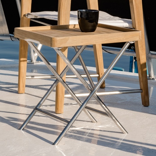 70460 Odyssey teak and stainless steel ottoman with teak serving tray and black coffee cup on top of tray next to the Odyssey folding chair on boat deck