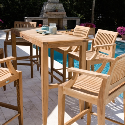 70501 Laguna 5pc teak Bar Set with plate and candle on pavers next to pool with fireplace two craftsman chairs two potted flowering plants and shrubs in background 