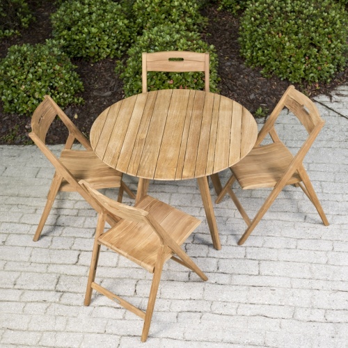 70519 Surf 5 piece teak round Dining Set of 4 folding side chairs and 42 inch round table on brick paver patio overhead view with landscape bushes in background
