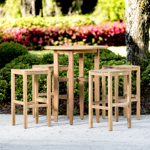 70533 Somerset Laguna 5 piece teak Bar Set of 4 teak backless barstools and round 36 inch diameter bar table on white brick patio with shrubs and flowers in background