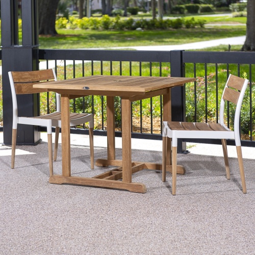70653 Bloom teak and cast aluminum 3 piece Dinette Set on covered patio against a black railing lined with shrubs showing a grass lawn and walkway and trees in background 