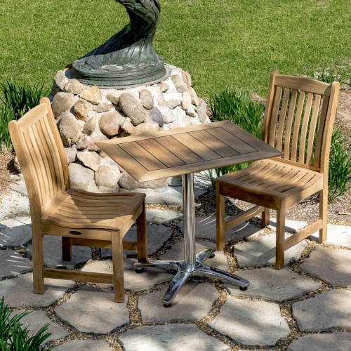 70669 Veranda Vogue Bistro Set of teak and stainless steel rectangular table and 2 teak dining chairs on stone patio with metal sculpture and grass lawn in background 