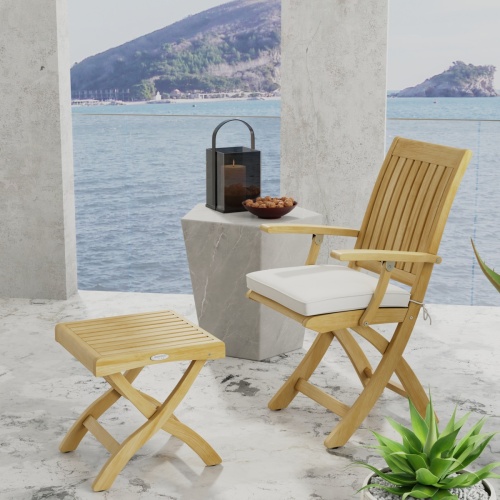 70799 Barbuda Chair and Ottoman Set showing Barbuda Chair with optional seat cushion and Ottoman in side angled view next to table with candle holder and bowl with ocean in back