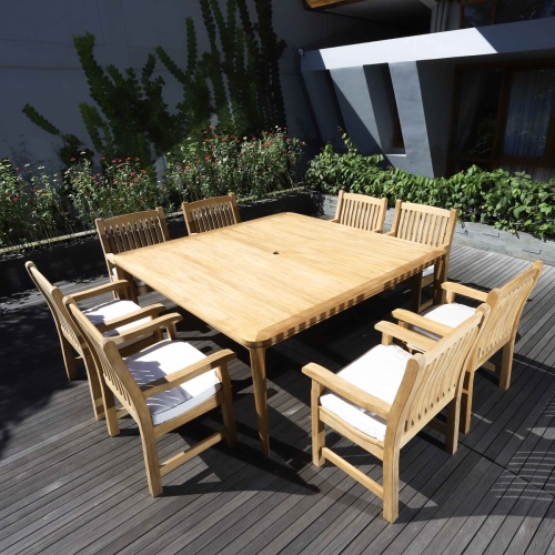 70878 Veranda 9 piece Square teak Dining Set with optional canvas colored seat cushions angled view on wood deck with flowers and house in background