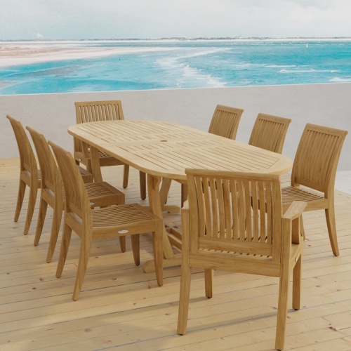 70926 Laguna Montserrat 9 piece Dining Set of Montserrat Oval Teak Table and 2 Laguna Dining Armchairs and 6 Laguna Side Chairs in angled end view on patio with ocean in background