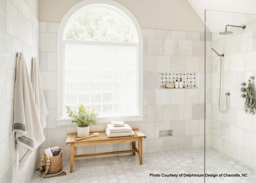 13916 Laguna teak backless bench in tiled bathroom shower with three folded towels back brush and plant on bench against window two towels on hooks toiletries in niche