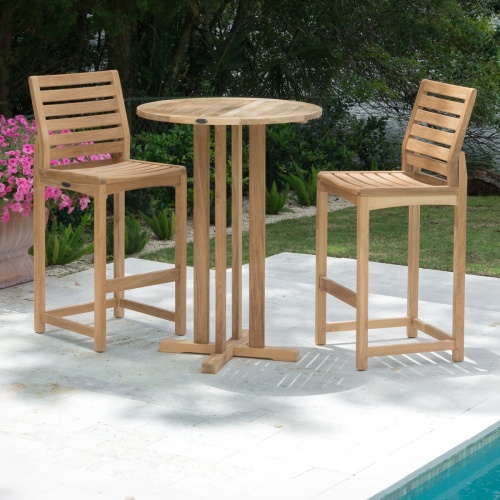 15033 Somerset teak Bar Table with 2 barstools on concrete patio next to pool flowering plant on side with grass landscape plants trees and lake in background