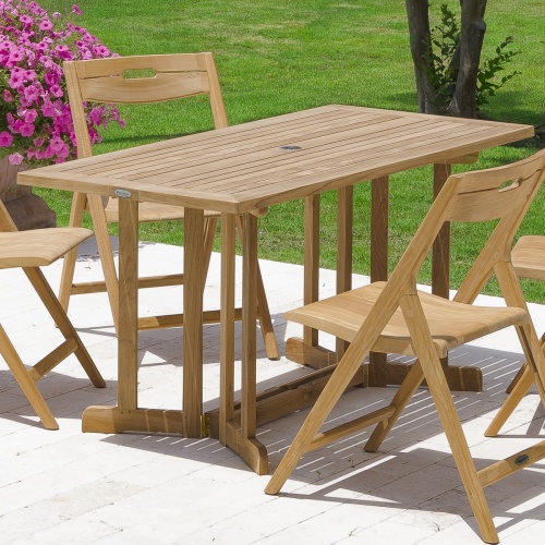 15663S Nevis teak 5 foot long folding Dining Table angled view on concrete patio with grass on right and flower on left