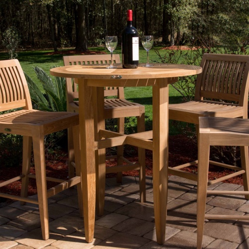 15817 Laguna 5 piece Teak High Bar Set with wine bottle and two wine glasses on stone patio with grass and trees in background