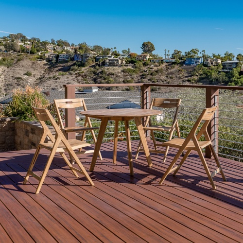70519 Surf 42 Inch Round Teak Dining Set on wood deck with landscape shrubs and ocean in the background