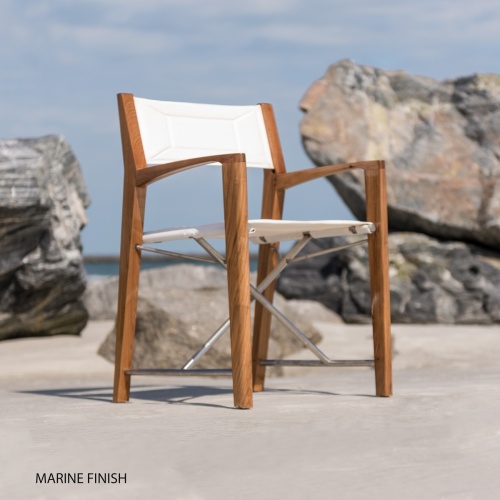 70459 Odyssey folding teak and stainless steel dining chair with Marine finish on beach with boulders and ocean and sky in background