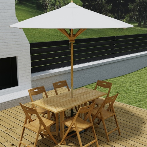 70472 Surf Nevis Teak 7 pc Dining Set with optional umbrella in angled aerial view on wood deck next to an outdoor fireplace with fence and hillside in background