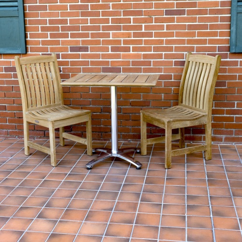 70669 Veranda Vogue Bistro Set of teak and stainless steel rectangular table and 2 teak dining chairs on outdoor tile patio with brick building and green window shutters in background 