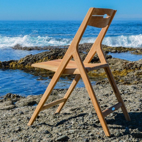 70677 surf teak folding chair on sand with ocean and blue sky background