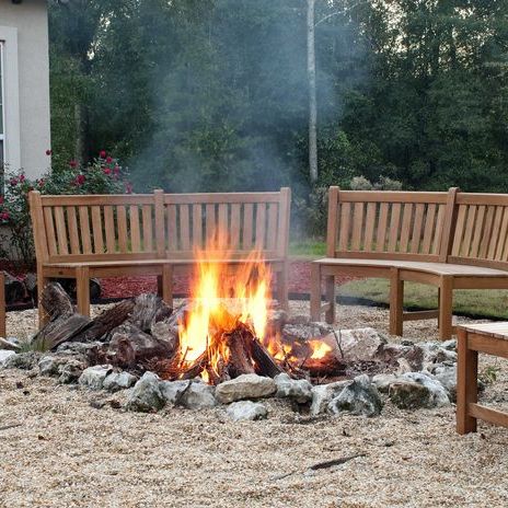70862 Buckingham teak 6ft curved bench set of 2 around fire pit with trees in background
