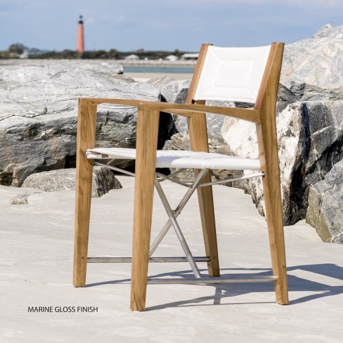 12915F Odyssey Folding Director Chair in marine gloss finish angled left side view on sandy beach by boulders with lighthouse homes beach and blue sky in background