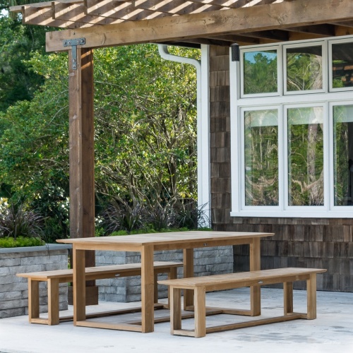 13909RF Refurbished Horizon teak 6 foot long Backless Bench angled view showing 2 with teak rectangular table on patio under a pergola with trees and house in background