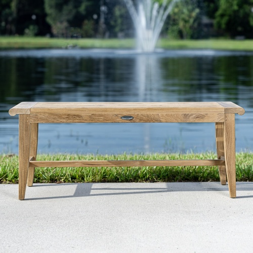13915 Laguna 4 foot long teak Backless Bench on concrete walkway with grass and lake with fountain in background