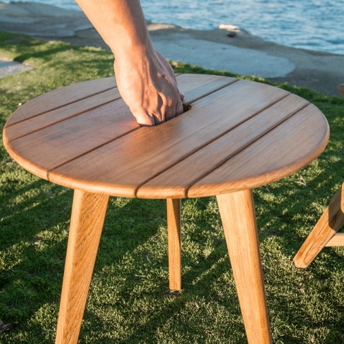14916 surf teak side table beside surf folding chair on sand by lake with boats and buildings in background