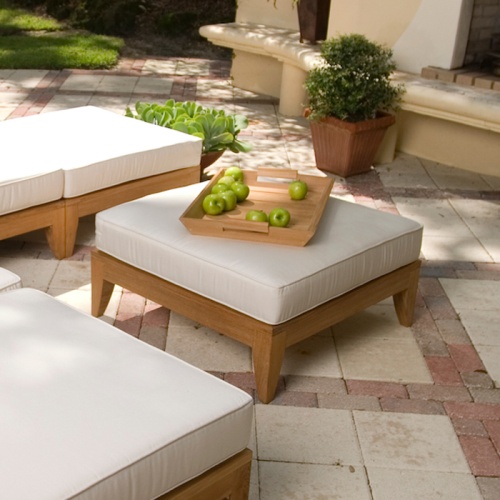 16767dp aman dais teak sectional ottoman fill teak base cushioned a teak tray with green apples on an outside paver patio with potted plants and a landscaped background