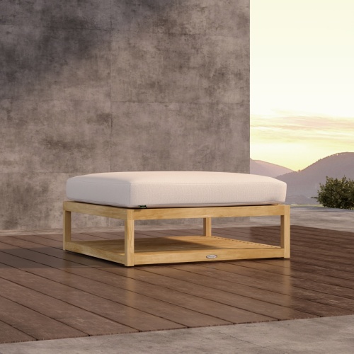 18800DP Maya Ottoman with cushion on wood patio in front of a partial privacy wall with hillside in background