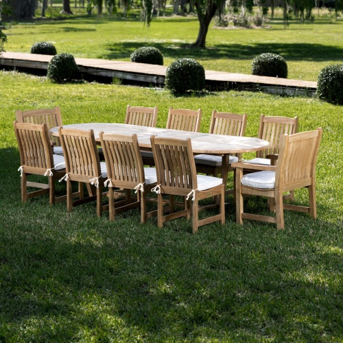 70008 Montserrat Veranda eleven piece oval dining set side view on a grass field with background of trees a boardwalk and lake 