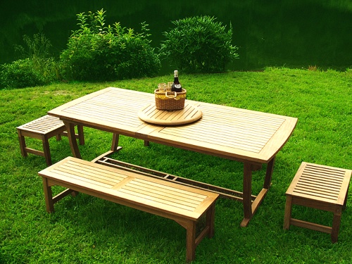 70009 Grand Veranda teak picnic table set a teak lazy susan with wine bottle and basket top angle view on a grass lawn and landscaped background