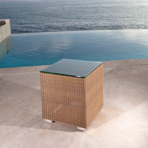  70242 malaga woven wicker glass top side table angle view on pool deck with infinity pool and ocean background