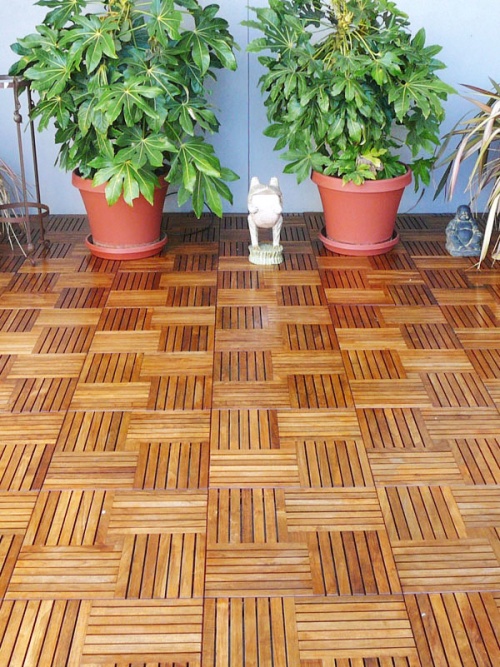 70405 Parquet 5 pack Teak 18 inch Deck Tiles on outdoor deck with 2 potted plants and landscape sculptures against a wall 