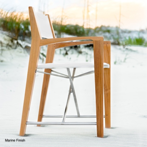 70459 Odyssey folding teak and stainless steel dining chair with Marine finish on beach with sea grass and sunset sky in background
