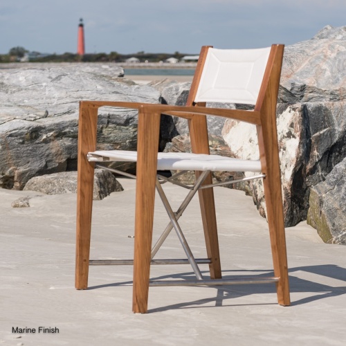 70558 Grand Hyatt Odyssey director chair facing left on sandy beach by boulders with lighthouse and ocean in background