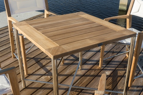 70595 Odyssey teak and stainless steel 32 inch square dining table on boat dock with marina in background