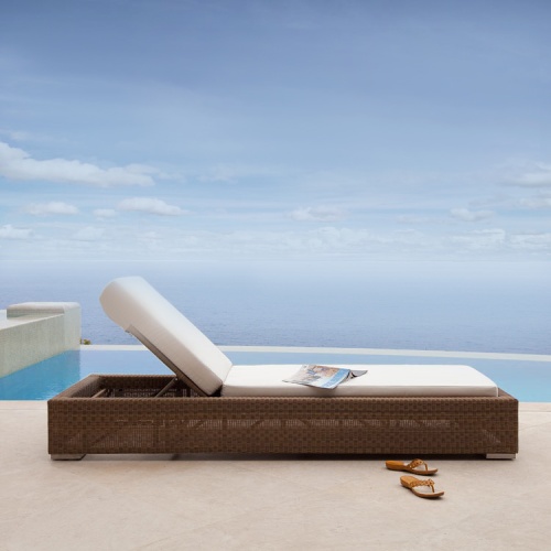 70656 Malaga synthetic wicker chaise lounger with cushions side profile with magazine lying open on chaise and sandals next to chaise on patio with pool and ocean background