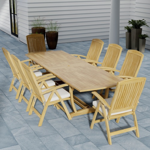 70796 Teak 9 piece Reclining Dining Set of 8 Barbuda reclining teak dining chairs with optional seat cushions and Grand Veranda teak extendable rectangular dining table in angled end view on slate tiled patio 5 potted plants against a house in the backgro