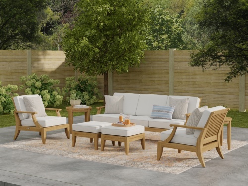 70871 Laguna 7 pc Conversation Set angled front view on outdoor patio with tray on ottoman and plant and books on side table with privacy fence and trees in background