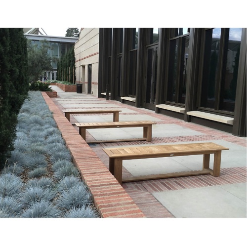 13909 Horizon teak 6 foot long Backless Bench showing three on concrete stone patio against brick planter with plants across windows in background