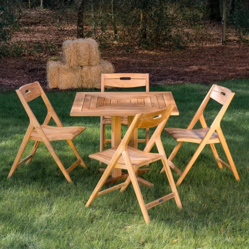 image of 70465 Surf Pyramid Teak Dining Set for 4 on grass field with bails of hey and trees in background