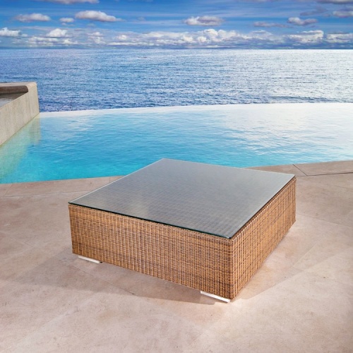 70259 malaga wicker coffee table with glass top angled on patio with pool ocean and blue sky in background