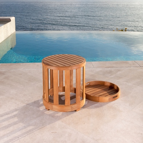 70271 Kafelonia round teak side table with teak tray lying on pool deck next to table with infinity pool ocean and blue sky in background