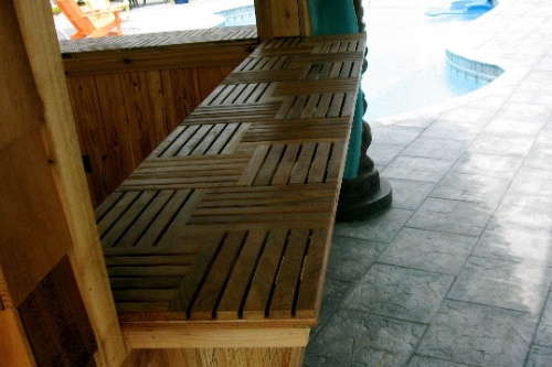 70403 parquet teak tiles on tiki bar counter on stone patio with pool in background